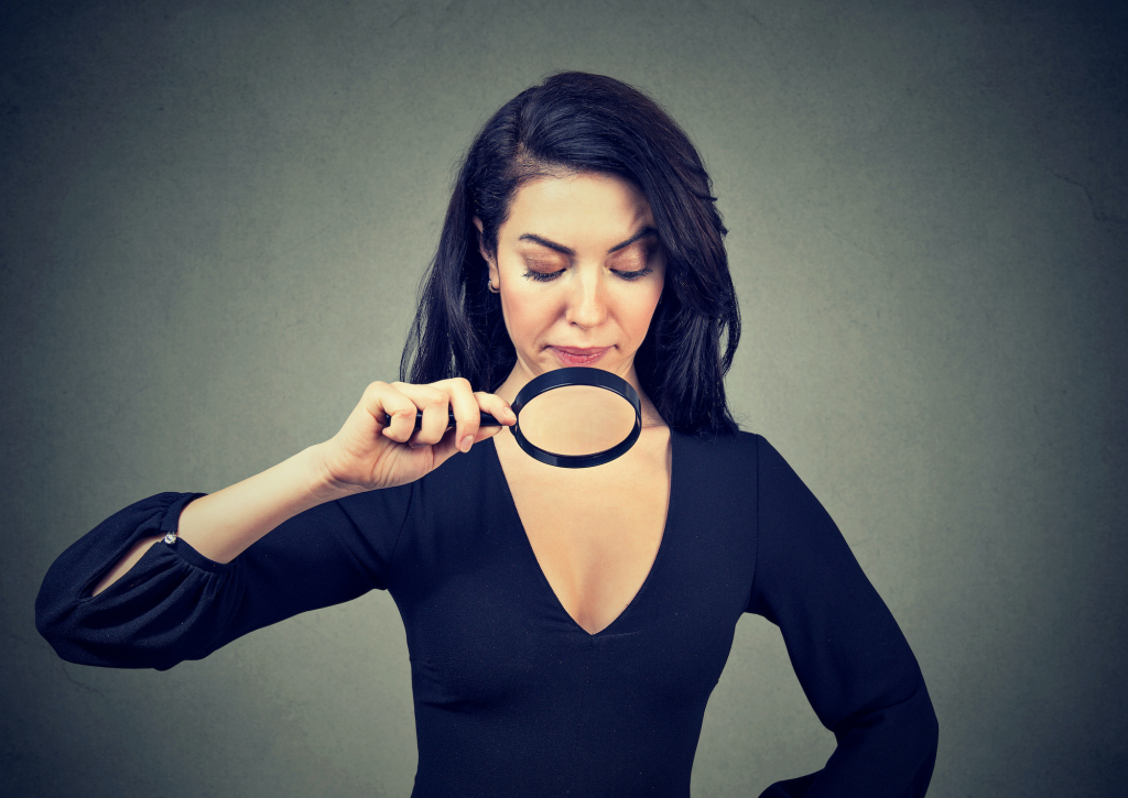 Young woman looking at her breasts through magnifying glass